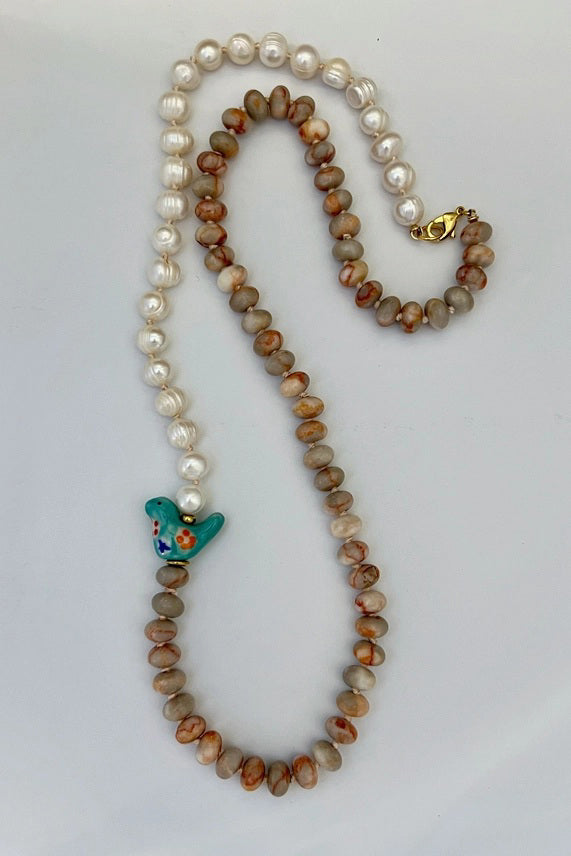 The GEMMA NECKLACE by SANDRINE FRANCE STUDIO features alternating freshwater pearls, round Red Vein Jasper beads, a blue ceramic bird bead, and a gold clasp. Handmade in NYC and shown against a plain white background.