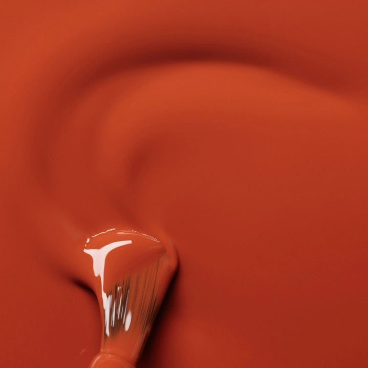 A hand with a glossy coat of MANUCURIST - GREEN™ NAIL POLISH IN TERRACOTTA by MANUCURIST INC touches an ear adorned with a chunky, abstract silver earring against brown skin.
