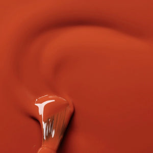 A hand with a glossy coat of MANUCURIST - GREEN™ NAIL POLISH IN TERRACOTTA by MANUCURIST INC touches an ear adorned with a chunky, abstract silver earring against brown skin.