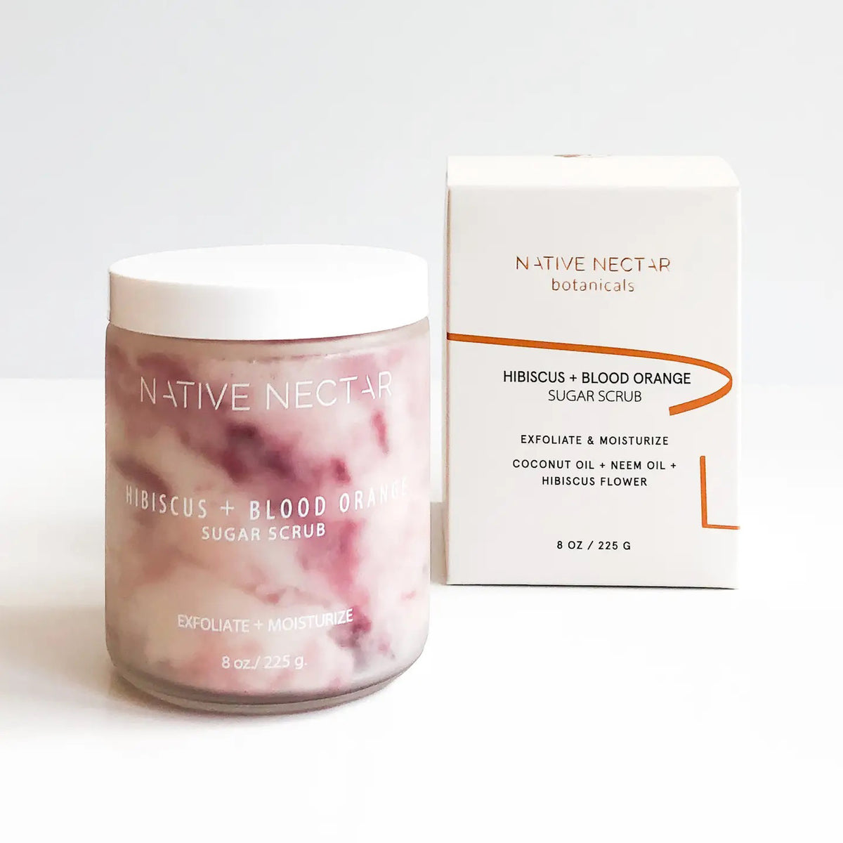 A jar and box of NATIVE NECTAR - HIBISCUS AND BLOOD ORANGE SUGAR SCRUB by NATIVE NECTAR sit side by side on a white surface, showcasing the marbled pink scrub perfect for glowing skin and a box listing key ingredients.