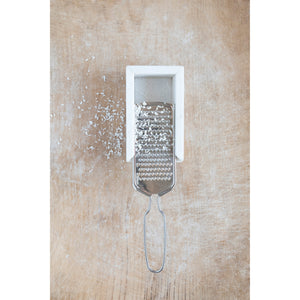 The CREATIVE COOP MARBLE AND STAINLESS STEEL GRATER, with its sleek handle and white marble rest, is shown from above, making it a stylish and modern addition to any kitchen countertop.
