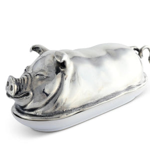 The VAGABOND HOUSE Pewter Happy Pig Butter Dish, a luxury-grade piece by VAGABOND HOUSE, gleams beside a white plate with butter and two slices, its lid open against a pristine white backdrop.