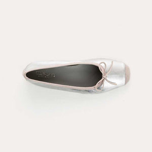 Top view of the REQINS - HARMONY BALLERINA FLATS IN METALIC SILVER by REQINS, featuring shimmering silver leather and a front bow, captured on a plain light background for a chic metallic look.