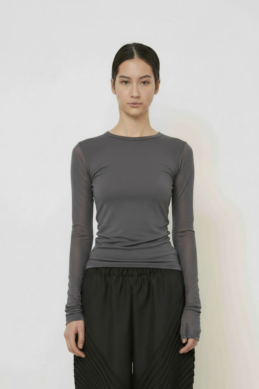 A woman with long dark hair in a low ponytail stands in profile against a plain light background, wearing the MEIMEIJ MESH LAYERING TOP by MEIMEIJ in red and a black skirt for a minimalist Italian fashion look.