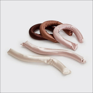 The KITSCH Satin Wrapped Flexi Rods 6 Piece Set by KITSCH features six vegan, satin-wrapped hair rollers in pink, beige, and brown tones. Displayed both inside their packaging and arranged in a fan shape outside, these flexi rods are perfect for creating beautiful heatless curls on curly or wavy hair.
