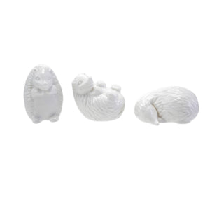 Six CREATIVE COOP WHITE STONEWARE HEDGEHOG figurines in different poses are arranged on and around three whitewashed cylindrical wooden pedestals, perfect for charming farmhouse decor. The background is plain white.