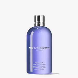 Three MOLTON BROWN Bluebell & Wild Strawberry Body Wash bottles are displayed on a light blue surface with a blue background, surrounded by strawberries and an applicator, evoking the floral-fruity fragrance to entice your senses.