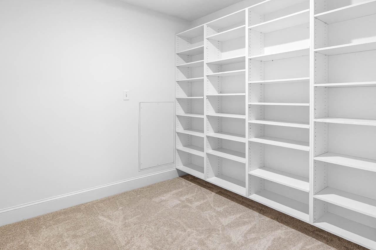 A room with beige carpet and empty white built-in shelving units along the wall, creating a clean and organized storage space.