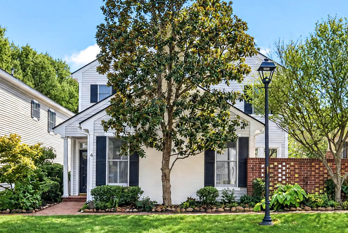 Two-story white house with dark shutters, a front porch, and a large magnolia tree in the yard.
