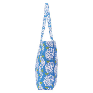 Carry your essentials in the ROCKFLOWERPAPER - HYDRANGEA LITTLE SHOPPER BAG, a stylish blue cotton canvas tote adorned with white hydrangeas and green leaves—an ideal grab-and-go accessory by ROCKFLOWERPAPER.