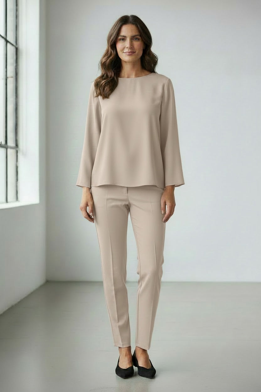 A person wears the MEIMEIJ TOP WITH KNOT BACK DETAIL in bright orange, paired with matching pants, standing against a plain light grey background. Their face is partially out of frame.