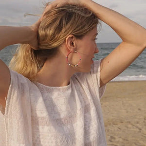 The ALICE RISE - BIG COLORLOOP EARRINGS IN SPRINGWATER by ALICE RISE feature two large hoops adorned with small, colorful Japanese glass beads, elegantly arranged and displayed on a textured light grey surface.