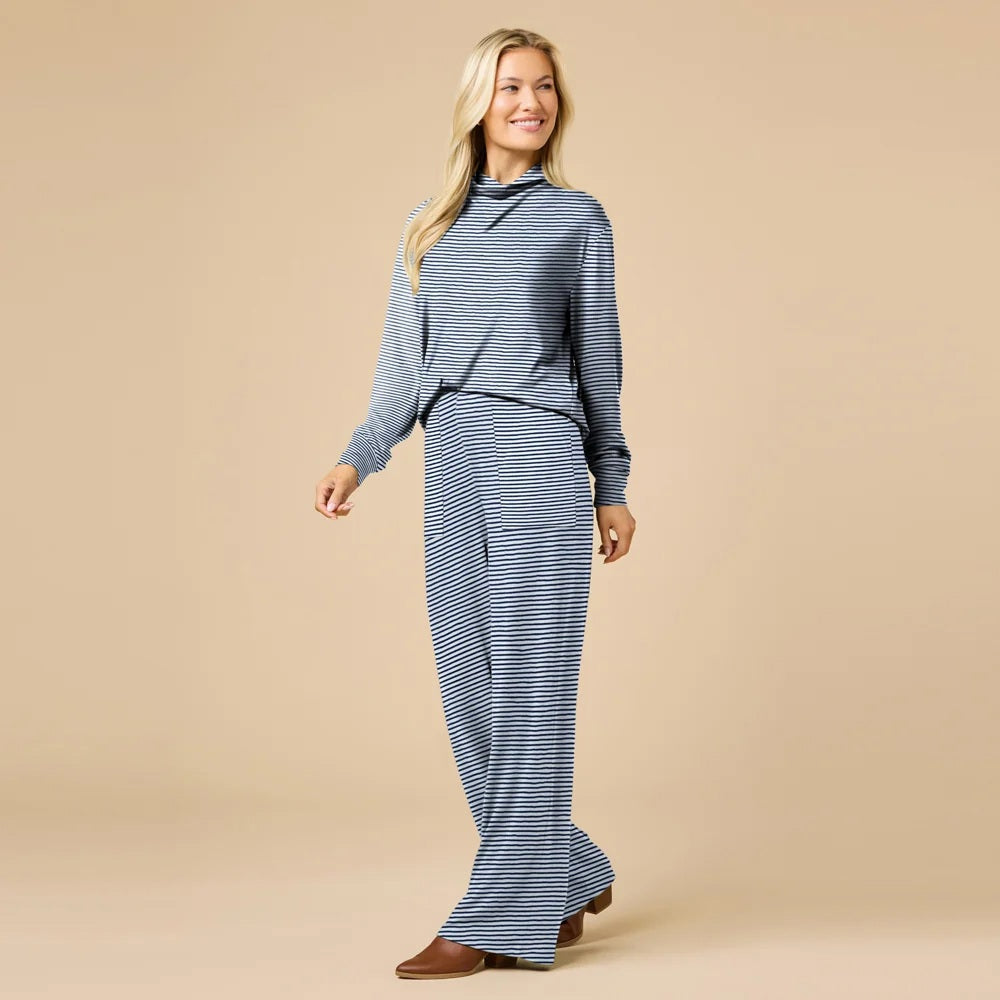 A woman wears a navy blue SOFTIES - DREAM JERSEY COWL NECK LOUNGE SET consisting of a long-sleeved top and wide-leg trousers.