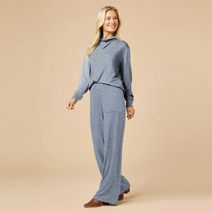 A woman wears a navy blue SOFTIES - DREAM JERSEY COWL NECK LOUNGE SET consisting of a long-sleeved top and wide-leg trousers.