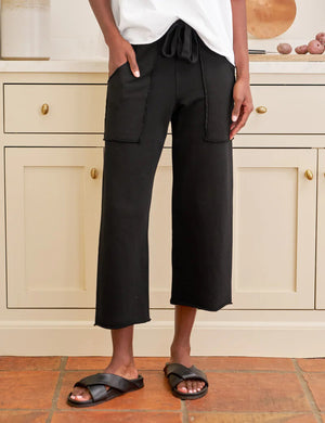 The FRANK & EILEEN Penny Patch Pocket Sweatpant in black features a cropped wide-leg style, elastic drawstring waistband, and large front patch pockets, crafted from cozy triple fleece and shown flat on a white background.