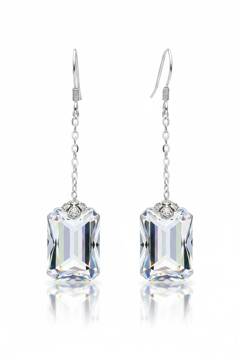 The VERDIER - SWAROVSKI EMERALD CUT CRYSTAL EARRINGS by VERDIER feature sterling silver hooks and rectangular, emerald cut crystals inspired by the Swarovski Aurora design, delicately suspended from fine chains and elegantly presented against a white background.