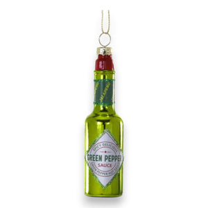 The CODY FOSTER GREEN PEPPER HOT SAUCE ORNAMENT is a shiny green glass decoration shaped like a hot sauce bottle, labeled "Green Pepper Sauce" with a gold hanging loop—ideal for collectors or as a unique gift.
