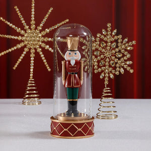 The SOLDIER IN CLOCHE by ZODAX is a decorative nutcracker with a white beard, red uniform, green pants, and gold accents, standing upright inside a clear glass dome on a red and gold base; battery operated for convenience.
