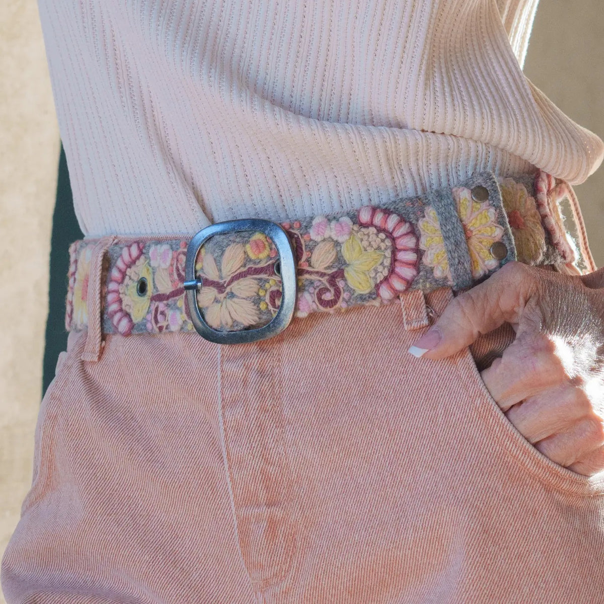 JENNY KRAUSS - HEATHER GRAY FLORAL EMBROIDERED WOOL BELT, coiled and handcrafted in Peru, featuring colorful floral embroidery and a dark metal buckle.