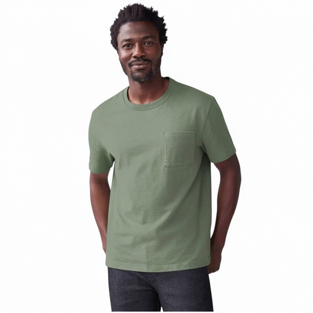 A person wears the MACK WELDON Heavyweight Slub Cotton Pocket T-Shirt in Cactus, a light olive green relaxed fit short-sleeve tee with a chest pocket, shown cropped to the upper torso against a plain white background.