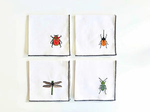 DOT AND ARMY’s EMBROIDERED INSECT COASTER set includes four linen/cotton coasters, each with a unique bug—red beetle, orange and black beetle, green dragonfly, and green bug—plus dark stitched edges, arranged on a white surface.