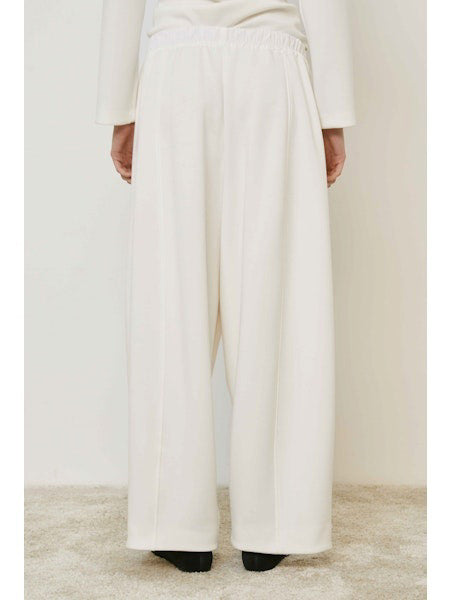 A person wears MEIMEIJ - PULL ON PANTS, featuring a wide-leg silhouette and elastic waistband, standing on a beige carpet in black shoes. These chic MEIMEIJ pants are made in Italy; the upper body is mostly out of frame.