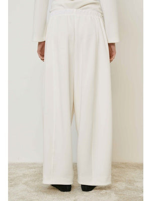 A person wears MEIMEIJ - PULL ON PANTS, featuring a wide-leg silhouette and elastic waistband, standing on a beige carpet in black shoes. These chic MEIMEIJ pants are made in Italy; the upper body is mostly out of frame.