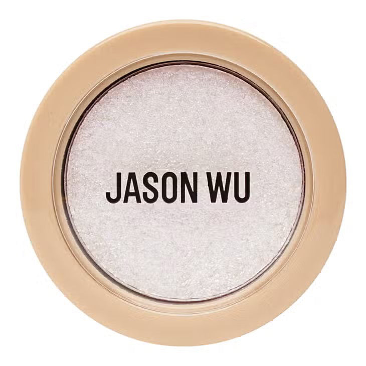 A small circular container of Jason Wu Beauty&#39;s &quot;Ready to Shimmer Ethereal 1&quot; eyeshadow. The cream eyeshadow is light-colored with an ethereal shimmer effect. The container features a beige-colored rim with the brand name &quot;JASON WU BEAUTY&quot; written in bold, black letters on the clear top.