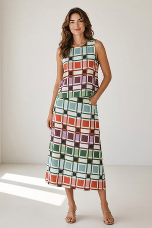 A woman wears a dark red knit poncho over a multi-colored BRITON COURT TIFFANY SKIRT IN CANDY BOX CHECK PLAID and brown sandals, perfect for a fall wardrobe.