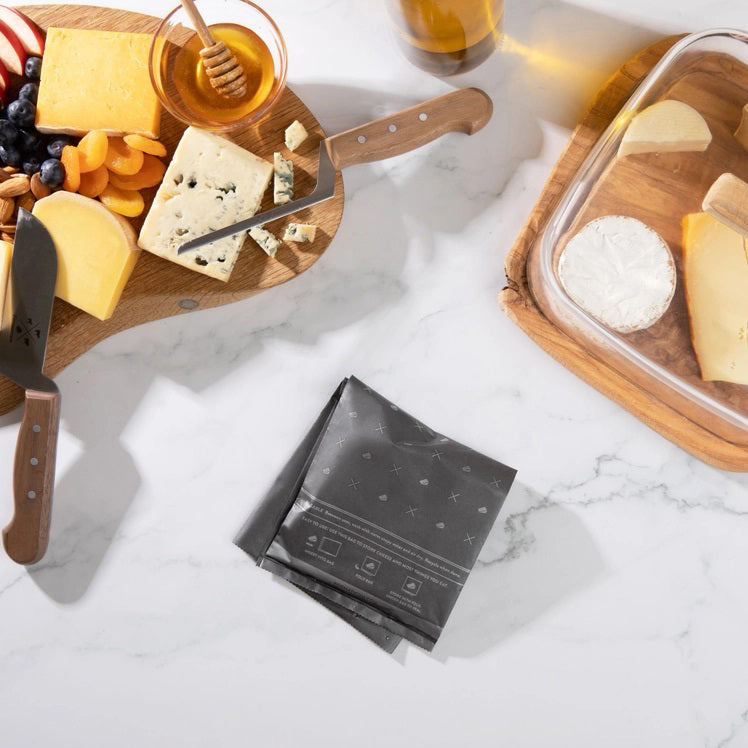A box of FORMATICUM - REUSABLE CHEESE STORAGE BAGS by FORMATICUM features a white and black design, “Reduce cheese waste” and “Keeps cheese fresher, longer” text, and contains 10 reusable bags.