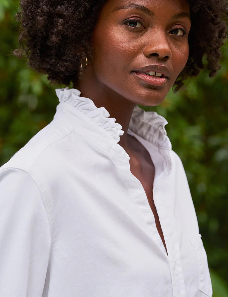 The FRANK &amp; EILEEN Ruffle Eileen Ruffle Collar Button Up Shirt in White Famous Denim features rolled-up long sleeves, a ruffled collar, and a single chest pocket, shown against a white background.