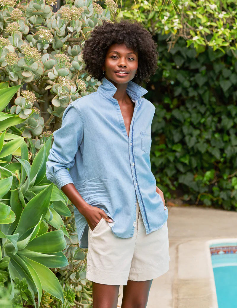 The FRANK &amp; EILEEN Eileen Relaxed Button Up in Famous Denim Classic Wash is a light blue, long-sleeve shirt with bust-flattering buttons, a chest pocket, rolled sleeves, and a curved hem, shown against a white background.