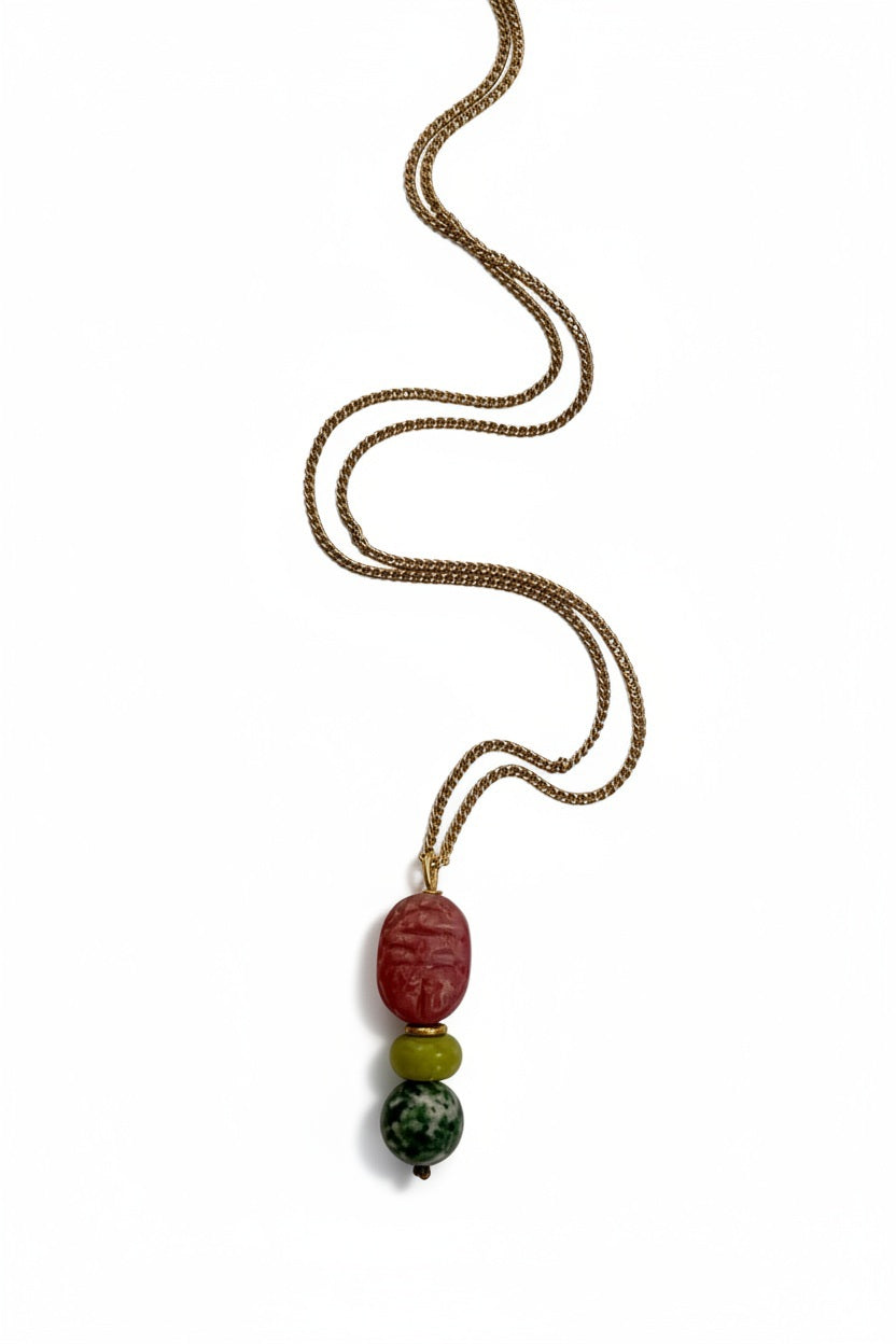 The SANDRINE FRANCE STUDIO - COMPANION WILLIAM NECKLACE by SANDRINE FRANCE STUDIO features a gold chain adorned with three beads: a large red Rhodonite Scarab bead at the top, a smaller yellow bead in the center, and a green speckled Tree Agate bead at the bottom, shown against a white background.