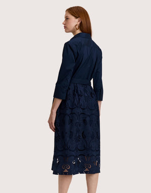 A woman stands against a plain light background wearing the HINSON WU Robin 3/4 Sleeve Eyelet Embroidery Dress in navy, featuring a collared neckline, belted waist, and an elegantly detailed lace-patterned skirt.