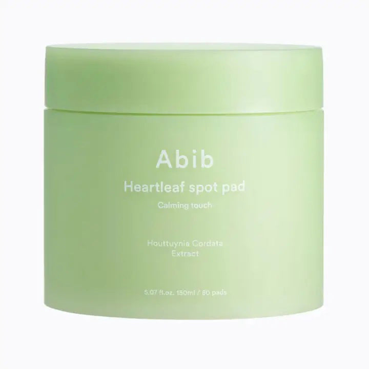 A light green jar labeled &quot;ABIB - HEARTLEAF SPOT PAD CALMING TOUCH 80 PADS&quot; from ASIAN BEAUTY WHOLESALE contains 80 pads with heartleaf extract and is shown against a plain white background.