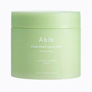 A light green jar labeled "ABIB - HEARTLEAF SPOT PAD CALMING TOUCH 80 PADS" from ASIAN BEAUTY WHOLESALE contains 80 pads with heartleaf extract and is shown against a plain white background.