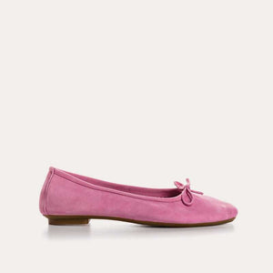 A close-up of the REQINS - HARMONY SUEDE BALLERINA FLATS IN PINK, featuring a bow detail on the front, photographed on a light surface—an elegant update to this classic women’s shoe by REQINS.