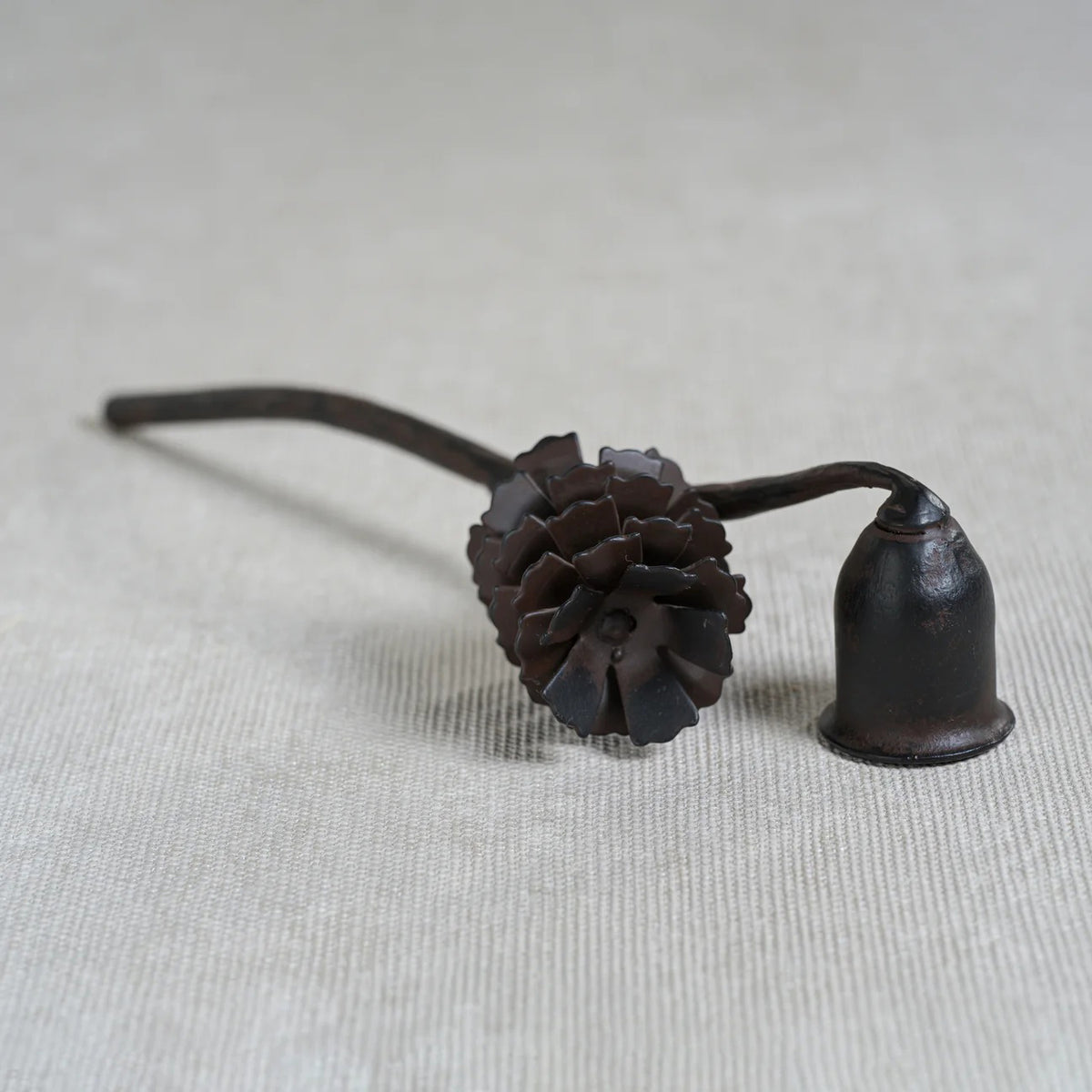 The ZODAX PINE CONE DESIGN WROUGHT IRON CANDLE SNUFFER features a sturdy dark metal build, a pinecone-shaped handle, and a bell-shaped tip, shown on a white background.