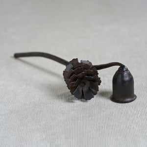 The ZODAX PINE CONE DESIGN WROUGHT IRON CANDLE SNUFFER features a sturdy dark metal build, a pinecone-shaped handle, and a bell-shaped tip, shown on a white background.