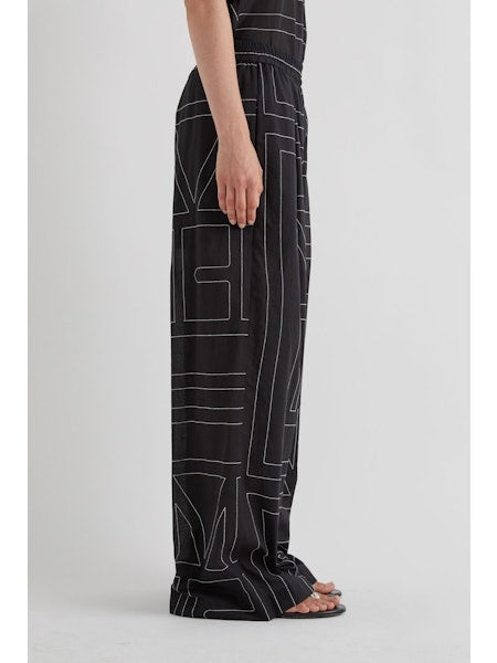 Model wears MEIMEIJ's ABSTRACT PRINT PANT—wide-leg black pants with a white abstract print—posing hands-in-pockets against a plain backdrop for a modern look.