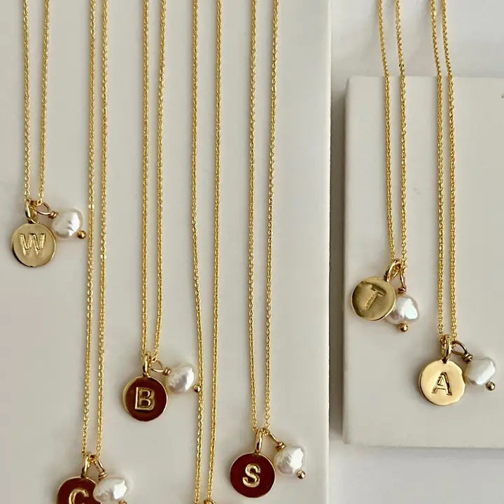 The SANDRINE FRANCE STUDIO TYPWRITER INITIAL NECKLACE &quot;E&quot; features a gold-plated, handmade round pendant engraved with an &quot;E&quot; and paired with a freshwater pearl charm, presented on a delicate chain.