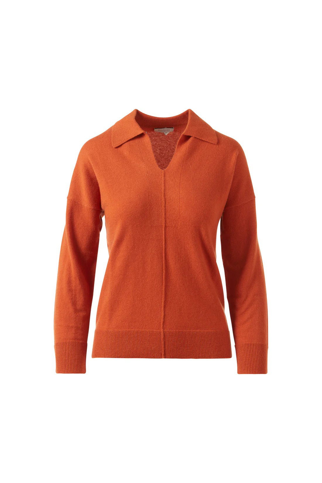 A woman stands against a white background, wearing the KINROSS CASHMERE Splitneck Polo in cashmere. She pairs it with matching pants, poses relaxedly while holding the hem of her top, and smiles softly.