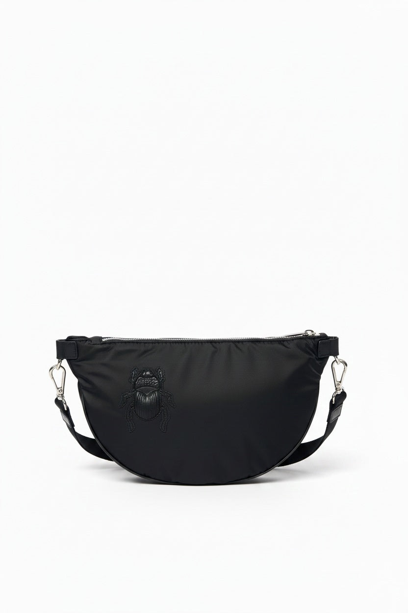 The GABRIELE FRANTZEN - SCARAB NYLON XL BELTBAG IN BLACK is a half-moon crossbody bag crafted from luxurious Italian nylon, featuring a matching black scarab beetle design on the front, silver-tone hardware, and an adjustable strap. This sleek nylon beltbag by GABRIELE FRANTZEN is displayed against a plain white background.