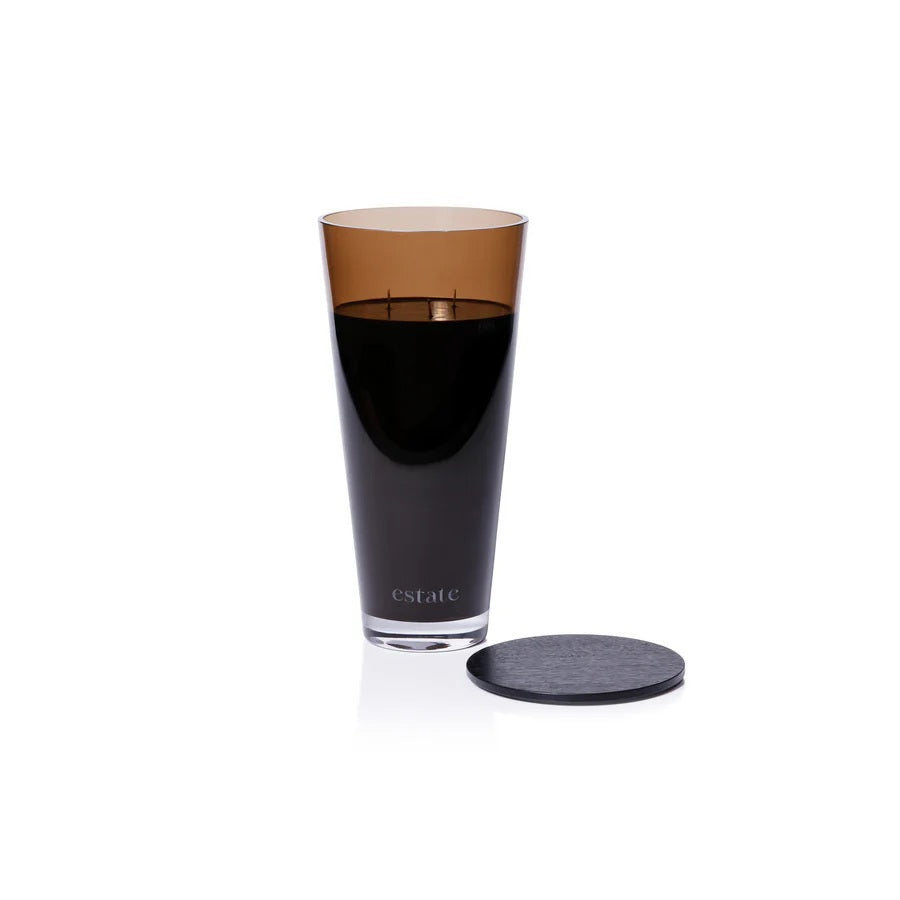 A collection of ZODAX luxury scented candles, including the 57 OZ THISTLE ESTATE CANDLE in black and smoky brown, is displayed on a white textured surface against a plain light background.
