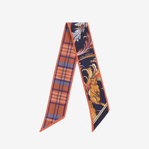 A hand wears the INOUI EDITIONS ROCOCO SQUIRREL SILK RIBBON by INOUI, its red, navy, and beige squirrel and foliage motif adding elegance to light beige pants and a black top.