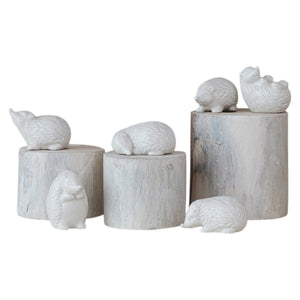 Six CREATIVE COOP WHITE STONEWARE HEDGEHOG figurines in different poses are arranged on and around three whitewashed cylindrical wooden pedestals, perfect for charming farmhouse decor. The background is plain white.
