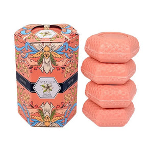 Hexagonal pink soaps with a honeycomb pattern are stacked beside a decorative orange and pink box labeled “BAUDELAIRE - ORANGE BLOSSOM HONEY SOAP 1.4 OZ QUARTET.” Each bar in this luxurious BAUDELAIRE set is triple-milled for rich lather and long-lasting Orange Blossom fragrance. The intricate floral designs on the box are complemented by a distinctive floral badge on top.