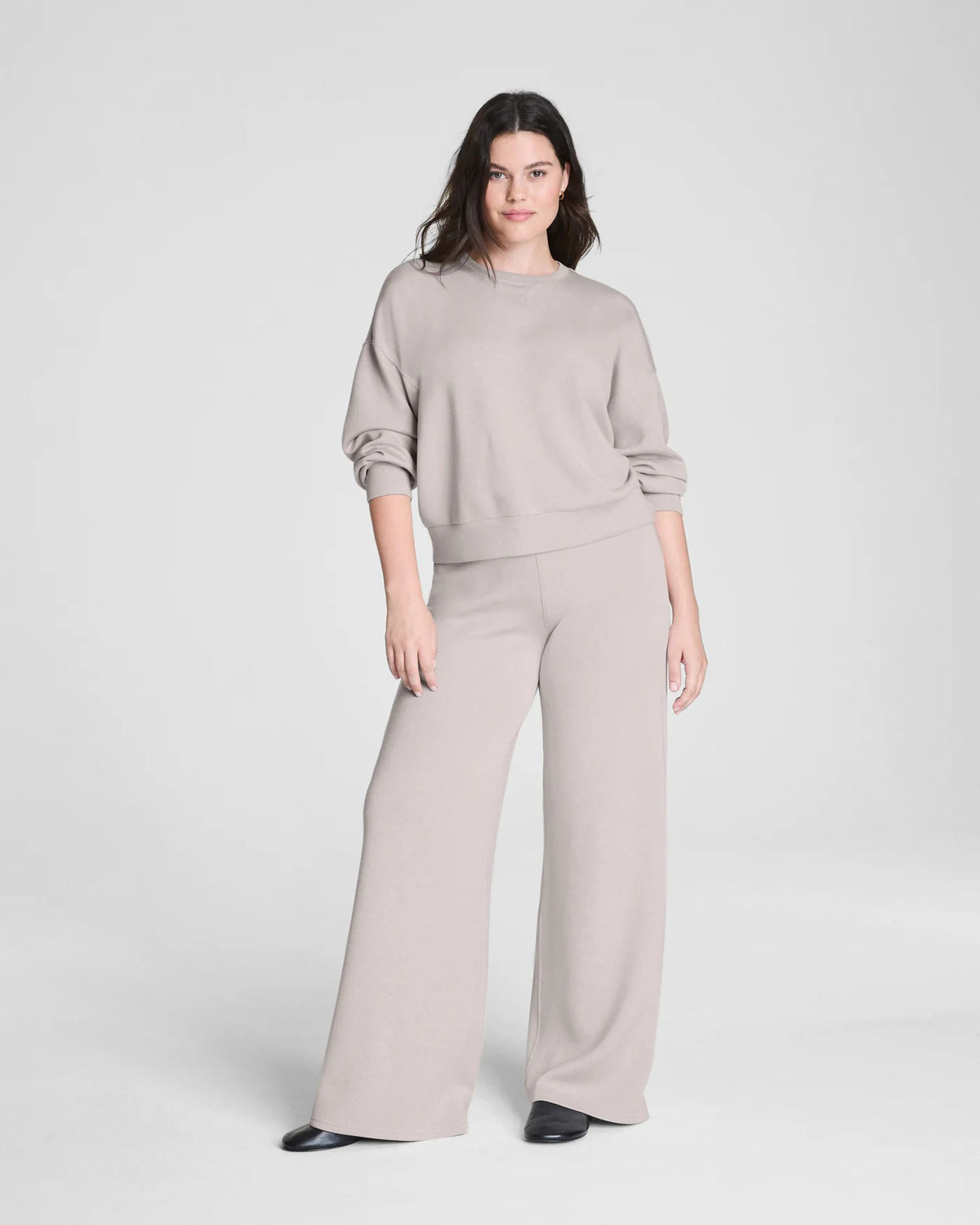 Someone stands facing away against a plain background, hands on hips, wearing SPANX - AIRESSENTIALS Wide Leg Pant in high-waisted, loose-fitting light beige and black shoes. The pants are crafted from airy fabric by SPANX.