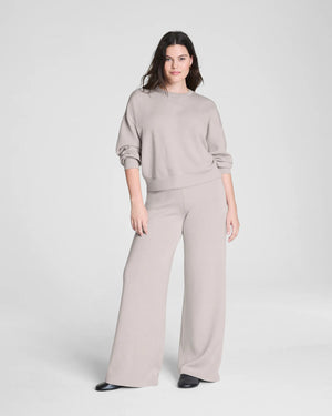 Someone stands facing away against a plain background, hands on hips, wearing SPANX - AIRESSENTIALS Wide Leg Pant in high-waisted, loose-fitting light beige and black shoes. The pants are crafted from airy fabric by SPANX.