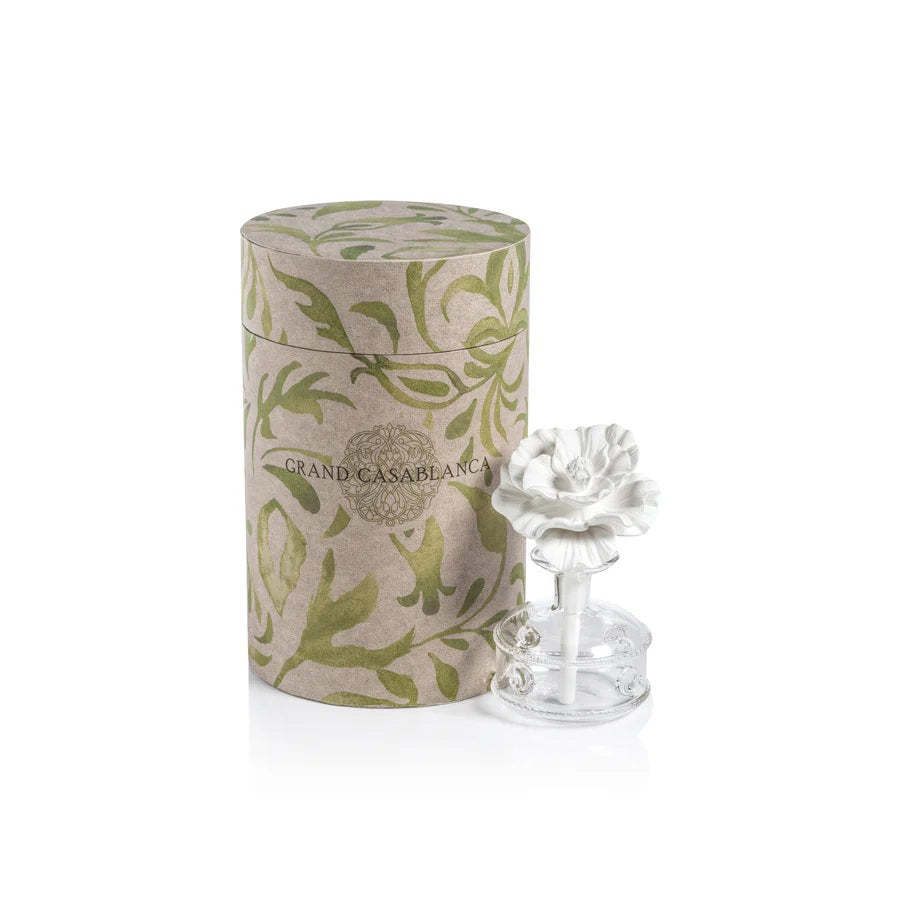 A set of MINI GRANDCASABLANCA PORCELAIN DIFFUSER - 1.7 OZ by ZODAX sit on marble; two display ceramic flower toppers, while others glow softly, filling the air with subtle wild tuberose notes.